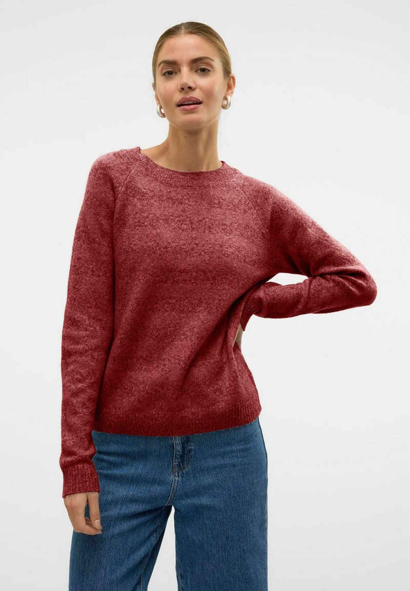 Pull en tricot rouge avec une finition texturée, col rond et poignets côtelés. Associé à un jean en denim bleu.