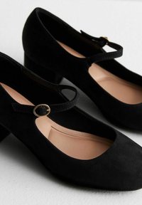 Zwarte suède Mary Jane-schoenen met een ronde neus, lage blokhak en een decoratieve band met een gouden gespdetail.