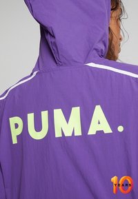 Purple hooded jacket with large "PUMA." logo in light green on the back, featuring white stripes along the shoulders. Light, textured fabric.