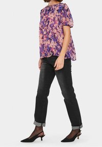 Lila och rosa blommig blus med korta puffärmar, tillsammans med svarta jeans som är rullade vid fållarna och svarta pumps med kitten-heel.