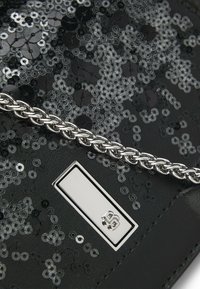 Mustalla paljeteilla varustettu clutch, jossa on hopeinen punottu ketjumme ja suorakulmainen metallinen yksityiskohta edessä. Pintakuvioinnit näkyvät.