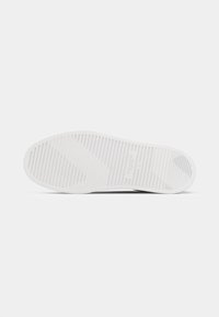 White sneaker sole featuring a flat design with horizontal ridges for traction, smooth surface, and slight curvature at the toe area.