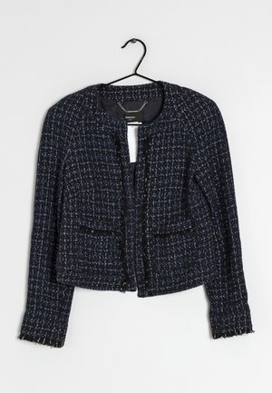 Dunkelblaue und schwarze Tweed-Cropped-Jacke mit langen Ärmeln und fransigen Säumen an einem schwarzen Bügel vor weißem Hintergrund.