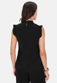 Schwarzes �ärmelloses Top mit Rüschendetails an den Schultern, hohem Halsausschnitt und einer Schlüssellochöffnung im Rücken. Glatte Stoffqualität mit taillierter Silhouette.