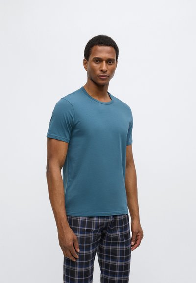 Turkio spalvos trumpomis rankovėmis marškinėliai su apvalia apykakle, pagaminti iš švelnios medžiagos. Modelis dėvi languotus pižamos kelnes tamsiai mėlynos ir baltos spalvų.