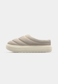 Beige slip-on sko med quilted overflate og teksturert overflate. Har en tykk hvit gummisåle og minimal merkevarebygging foran.