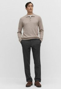 Valkoinen beige neulepaita kauluksella ja kolmella napilla, yhdistettynä tummanharmaisiin housuihin. Teksturoitu kangas ja ruskeat kengät viimeistelevät asun.