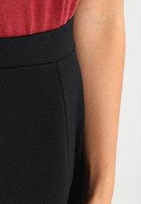 Svart texturerad högmidjad kjol med en slät midjeband och subtilt vävt mönster, ihopparad med en röd kortärmad topp.