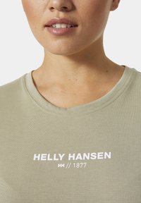 Světlonzelené tričko s kulatým výstřihem, vyrobené z měkké tkaniny, se bílým textem a logem "HELLY HANSEN" umístěným na hrudi.