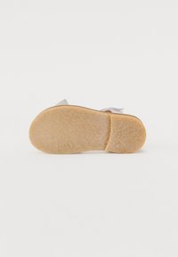 Semelle en caoutchouc marron avec finition texturée, tige en tissu gris clair avec un design en couches, dos ouvert, accent subtil de boucle sur le talon.