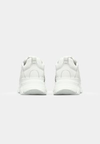 Chaussures de sport blanches avec une tige en cuir lisse, un col rembourré, des coutures contrastées et une semelle épaisse texturée pour une meilleure adhérence.