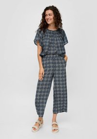 Marineblauw jumpsuit met korte mouwen en elastische taille, voorzien van geometrische patronen. Draag het met lichtgekleurde platform sandalen.