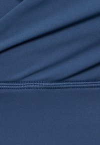 Marinblå sträckt tyg med en slät yta, med en vikt design och synliga sömmar längs fållen.