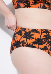 Parte inferiore di bikini a vita alta in tessuto arancione con stampa di palme nere. Texture liscia e cuciture rinforzate lungo i bordi.