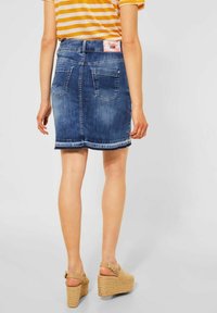 Jeanskjol i mörkblått med fransad nederkant, två bakfickor och en märkeslapp vid midjan. Bärs med bruna platåsandaler.