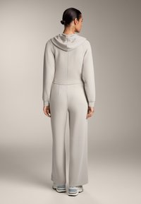 Salopette grigia chiara con cappuccio, caratterizzata da maniche lunghe e pantaloni a gamba larga, realizzata in tessuto morbido. Design semplice senza motivi visibili.