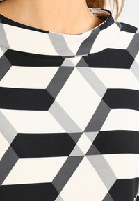 Mönstrad topp med geometrisk design i svart, vitt och grått. Mjuk tygkvalitet med hög halsringning och slät textur.