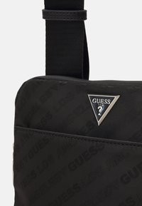 Borsa a tracolla in nylon nero con motivo a tonalità del logo "GUESS", tracolla regolabile e accento con logo triangolare in argento. Texture liscia su tutta la superficie.