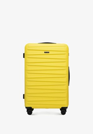 Valise rigide jaune avec texture à nervures horizontales, poignée rétractable et quatre roues pour la mobilité. Logo de la marque centré à l'avant.