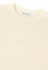 Felpa a girocollo color crema realizzata in tessuto morbido con collo e polsini a costine. Presenta un ricamo sottile "Oh April" sul davanti.