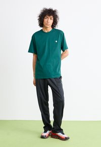 Green short-sleeve t-shirt with a small logo, paired with black athletic pants and multi-colored running shoes with a distinct design.