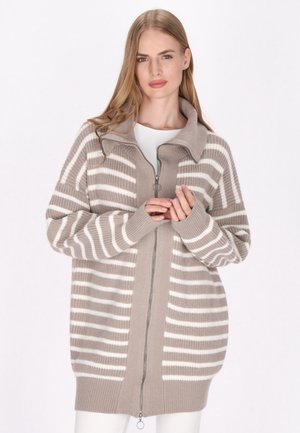 Cardigan oversized bej cu dungi orizontale albe, cu fermoar frontal, guler înalt și manșete dantelă. Textură moale, tricotată.