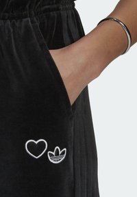 Svarta sammetsbyxor med sidoficka, vit broderad hjärt- och logodetaljer. Texturerad tyg med elastisk midja.