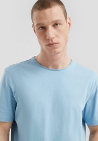 Jasnoniebieska koszulka z krótkim rękawem, wykonana z gładkiego materiału, z okrągłym dekoltem i luźnym krojem. Brak widocznych wzorów lub akcentów.