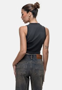 Top corto senza maniche nero con una texture liscia abbinato a jeans a vita alta sbiaditi blu, caratterizzati da una toppa in pelle marrone con logo sul retro.