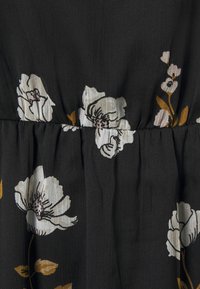 Czarna tkanina z kwiatowym wzorem w białe i złote kwiaty. Tkanina ma pomarszczoną teksturę i jest zebrana w pasie.