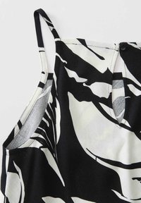 Top sans manches à motif abstrait noir et blanc avec une petite encoche et un détail bouton au niveau de l'encolure.