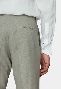 Hellgraue Hose aus strukturiertem Stoff, ausgestattet mit einer Gesäßtasche, getragen mit einem weißen Leinenhemd. Sichtbare Knopfdetails an den Ärmeln.