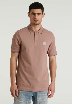 Polo shirt rosa chiaro con colletto, maniche corte, tre bottoni e un piccolo logo sul lato sinistro del petto. Indossato con jeans blu strappati.