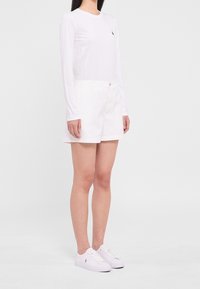 Chemise blanche à manches longues, short blanc et baskets blanches. La chemise présente un petit logo ; le short a une coupe classique avec des poches.