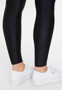 Svarta, åtsittande leggings i ett mjukt, sträckt material. Matchas med vita kanvas sneakers med låg profil och diskret branding.