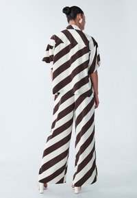 Kurzmantel mit kurzen Ärmeln und Hose mit weiten Beinen im Creme- und Braunstreifen-Design, aus leichtem Stoff hergestellt, mit lockerer Passform und dezentem Glanz.