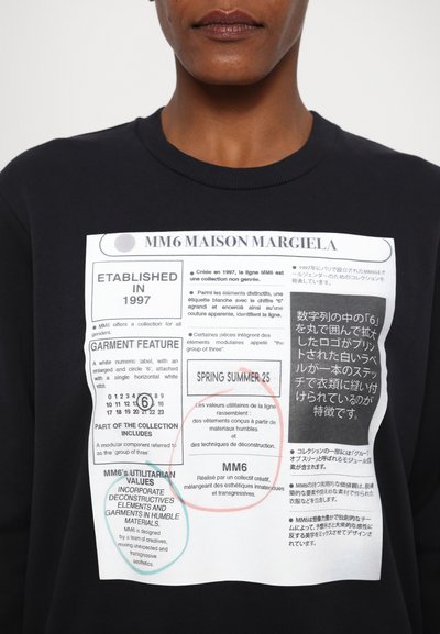 Μαύρη φούτερ μπλούζα με μεγάλη λευκή ετικέτα γραφικών που περιλαμβάνει κείμενο και αριθμητικές λεπτομέρειες, καθώς και σχεδιαστικά στοιχεία σε μπλε και κόκκινους κύκλους.