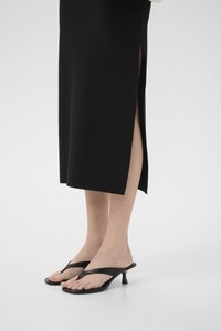 Black heeled flip-flops with a minimalist design, featuring thin straps and a contoured footbed, paired with a black midi skirt with side slits.