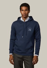 Sudadera azul marino fabricada en suave algodón, con un bolsillo frontal, capucha con cordón y logo bordado en el pecho.