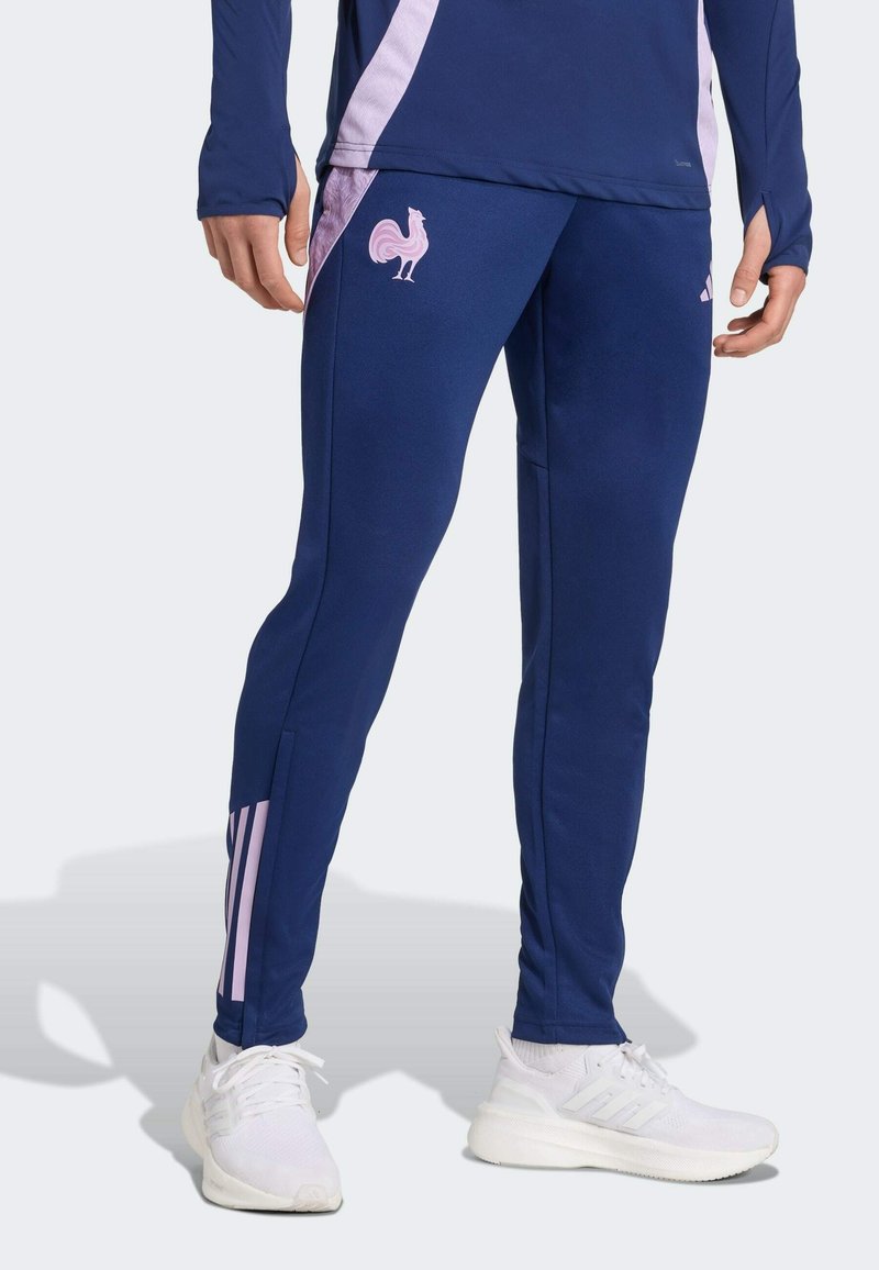 Pantalons de sport navy avec un logo de coq rose sur la cuisse gauche, présentant un design fuselé et des bandes d'accent rose sur le bas de la jambe.