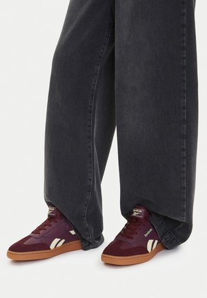 Bordeauxrote Sneaker aus Wildleder und Leder, mit weißen Akzenten und einer Gummisohle, kombiniert mit weiten grauen Denim-Hosen.