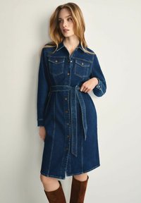 Sukienka koszulowa z denimu w ciemnoniebieskim kolorze, z długimi rękawami, dwiema kieszeniami na piersi, paskiem w talii oraz zapięciem na guziki, z linią A.