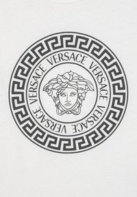Bílý tričko s černým kruhovým motivem, uprostřed s hlavou Medusy a opakovaným textem "VERSACE", obklopené vzorem řeckého klíče.