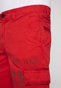 Rode cargoshorts van lichtgewicht stof met een knoopsluiting, zijzakken en een bedrukt tekstdetail langs de dij.