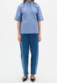 Blårandig kortärmad topp med hög krage, ihop med löst sittande blå denimbyxor. Skorna är svarta med en spetsig tådesign.