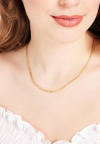 Collier en chaine dorée porté autour du cou, présentant un design de maillons simple avec une finition lisse, reposant sur un haut blanc légèrement froncé.