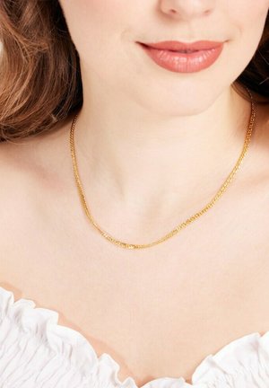 Gouden ketting om de hals, met een eenvoudig schakeldesign en een gladde afwerking, rustend op een zacht gerimpeld wit topje.
