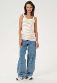 Débardeur à rayures beige et crème, associé à un jean clair à jambes larges. La tenue présente un design décontracté avec une coupe oversize.
