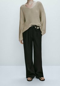 Beige knitted sweater with a loose fit, paired with high-waisted black wide-leg trousers. Black belt and flat sandals complete the outfit.