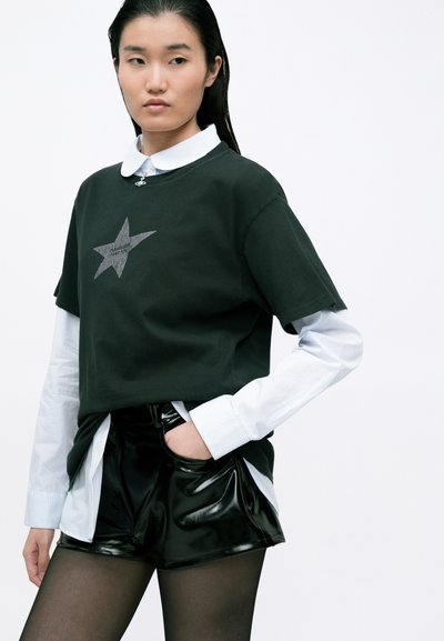 Tricou negru din bumbac, cu un design scurt și imprimeu cu stele gri, purtat peste o cămașă albă cu guler, asortat cu șorturi negre lucioase.